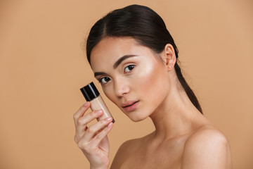 Beauty portrait closeup of brunette asian woman with makeup looking at camera and holding concealer...