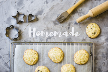 Word Homemade is written on a gray concrete background of flour. Next to the baking sheet with biscuits, shapes and rolling-pin. Homemade pastry concept. Top view, flat lay