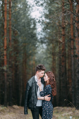 Young stylish couple in the forest, running around the Park and laughing. Modern people on a walk. Beautiful girl with tattoos. Loving young man and girl. mountain Park with pine forest