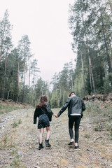 Obraz premium Young stylish couple in the forest, running around the Park and laughing. Modern people on a walk. Beautiful girl with tattoos. Loving young man and girl. mountain Park with pine forest