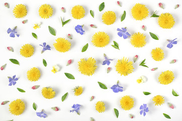 Obraz premium Floral pattern made of yellow dandelion, lilac flowers, pink buds and green leaves isolated on white background. Flat lay. Top view.