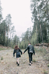 Young stylish couple in the forest, running around the Park and laughing. Modern people on a walk. Beautiful girl with tattoos. Loving young man and girl. mountain Park with pine forest