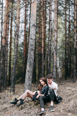 Fototapeta premium Young stylish couple in the forest, running around the Park and laughing. Modern people on a walk. Beautiful girl with tattoos. Loving young man and girl. mountain Park with pine forest