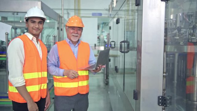 Senior quality inspector teaching junior team member in factory. Chinese old male with his young team discussing quality issue with bottle production line in background.