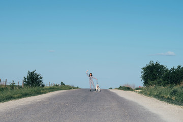 A pretty girl leads a dog next to her on the road