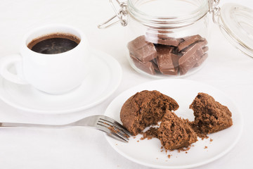 Chocolate muffin broken open on a plate, black coffee and pieces of chocolate in a jar. Selective focus