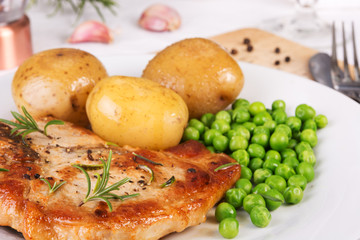 Close up of pork chop, boiled jacket potatoes and green peas served on a plate. Selective focus
