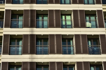 Fototapeta na wymiar Rows of apartment balconies with glass railing and brown wooden blinds.