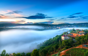 Dawn on plateau in morning with colorful sky, while sun rising from horizon shines down to small village covered with fog shrouded  landscape so beautiful idyllic countryside Dalat plateau, Vietnam