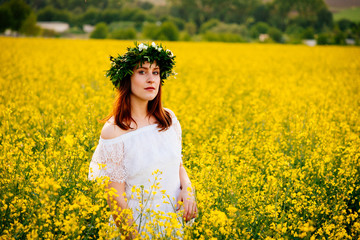 Fototapeta premium Young woman in white dress in a yellow rape field