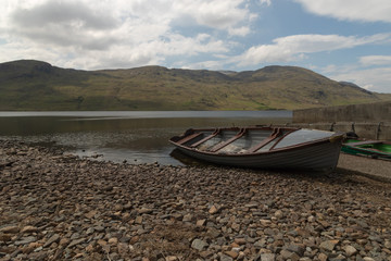 Abandonedwooden fishing boat the edge of a mountain lake, tranquil rural scene, summertime