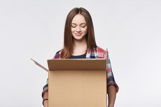 Delivery, relocation and unpacking. Smiling young woman holding carton box looking in box