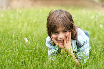 The  boy blond, dressed in a blue striped shirt, lies on the grass, leaning his head on his hands, he smiles.