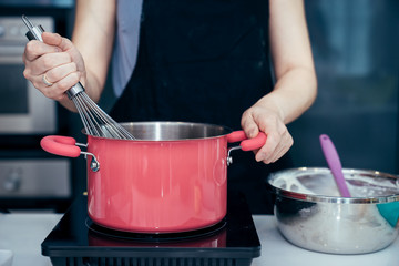 Asian women are chief stirring the ingredients of cake in pink stainless steel pot on an electric stove to making the birthday cake in a family weekend.