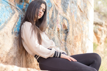 young woman sitting on a wall in a casual pose with intense gaze