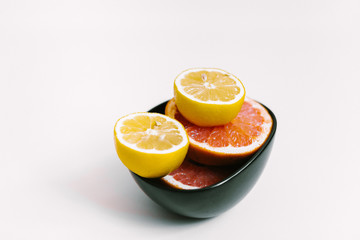 Fruit background. Colorful fresh lemons and grapefruit on a black plate on white table. Flat lay, top view, vertical orientation