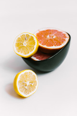 Fruit background. Colorful fresh lemons and grapefruit on a black plate on white table. Flat lay, top view, vertical orientation