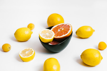 Fruit background. Colorful fresh lemons and grapefruit on a black plate on white table. Flat lay, top view, vertical orientation