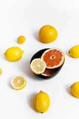 Fruit background. Colorful fresh lemons and grapefruit on a black plate on white table. Flat lay, top view, vertical orientation