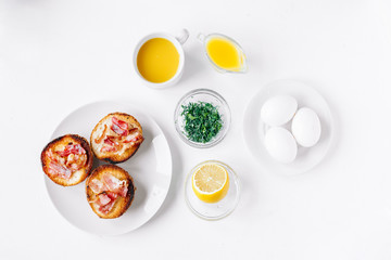 Ingredients for eggs Benedict bun with bacon, lemon, sauce, coriander top view