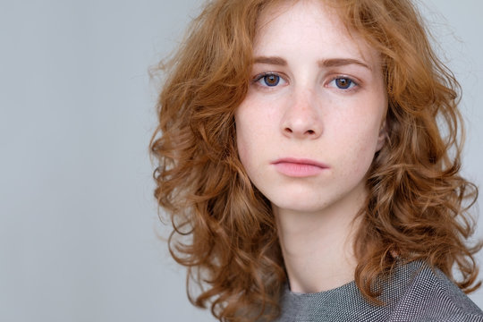 Portrait of young tender redhead teenage girl with healthy freckled skin wearing official dress looking at camera with serious or pensive expression.