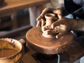 The potter's hands are shaped a cup from a clay. The process of creating pottery on a potter's wheel. The master ceramist works in his studio. Close-up, only hands. Crockery from clay own hands
