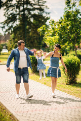 Obraz premium Happy joyful young family father, mother and little daughter having fun outdoors, playing together in summer park, countryside. Mom, Dad and kid laughing and hugging, enjoying nature outside