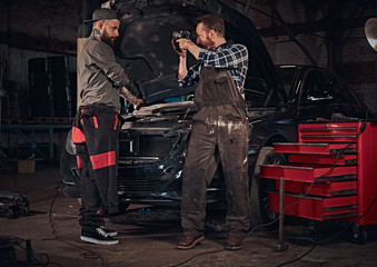Fototapeta na wymiar Two bearded auto mechanic in a uniform, repair a broken car in the garage. 