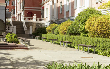 A paved stepped alley trail in a beautiful park framed with cut bushes and benches for rest