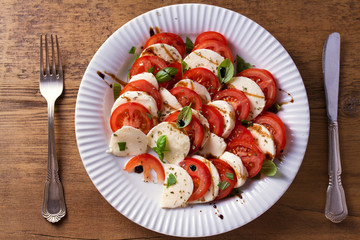 Italian caprese salad with sliced tomatoes, mozzarella cheese, basil, olive oil and balsamic vinegar. View from above, top studio shot