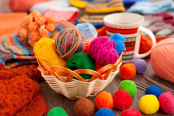 Colorful balls of yarn for knitting. Balls of yarn in a wicker basket. Knitting needles and threads for knitting of clothes. A cup of tea for coziness.