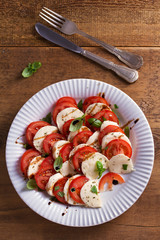 Italian caprese salad with sliced tomatoes, mozzarella cheese, basil, olive oil and balsamic vinegar. View from above, top studio shot