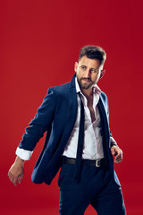 Male beauty concept. Portrait of a fashionable young man with stylish haircut wearing trendy suit posing over red background.