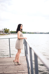 Young woman walks along waterfront. Brunette woman in gray summer dress