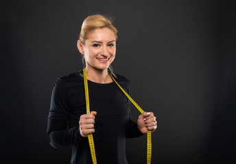 Pretty gym female trainer holding measuring tape and smiling.