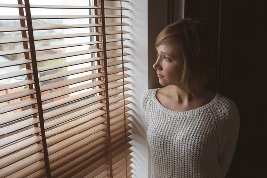 Young woman looking through window blind