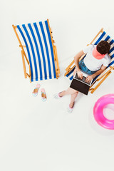 overhead view of woman sitting in beach chair and using laptop isolated on white
