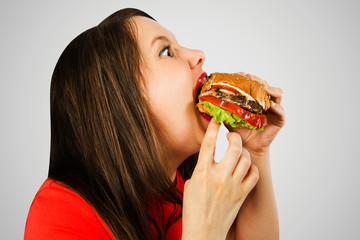 Young girl eats hamburger on gray background. Side view