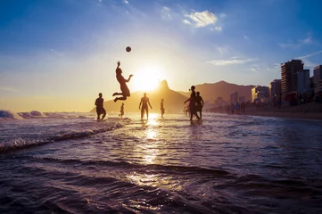 Gordijnen sunset silhouettes playing keepy-uppie beach football on the sea shore in Ipanema Beach Rio de Janeiro Brazil © lazyllama