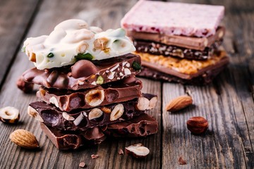 Stack of white, milk and dark chocolate with nuts, caramel and fruits and berries on wooden background.