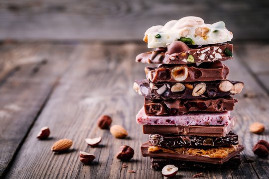 Stack of white, milk and dark chocolate with nuts, caramel and fruits and berries on wooden background.