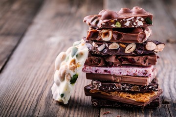 Stack of white, milk and dark chocolate with nuts, caramel and fruits and berries on wooden...