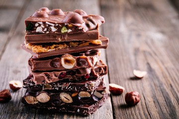 Stack of  milk and dark chocolate with nuts, caramel and fruits and berries on wooden background.