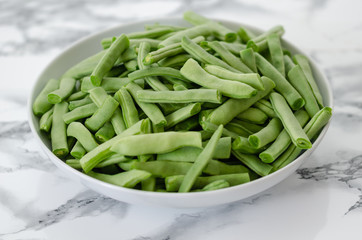 Green beans in the white plate on  grey and white background.