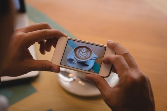 Businessman clicking photo of coffee in coffee shop