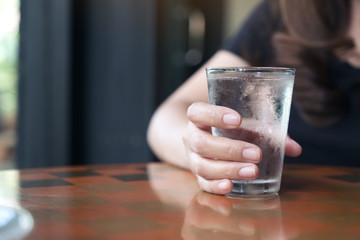 Closeup image of woman's hand holding a glass of cold water on table