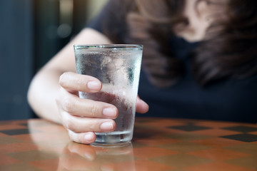 Closeup image of woman's hand holding a glass of cold water on table