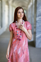 Young beautiful girl posing in seamless dress made in author's technique from merino wool in pink-peach scale, closeup