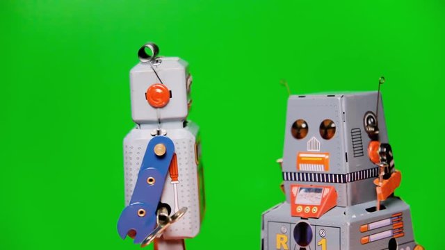 Two tin toy robots clashing into each other, over a green background.
