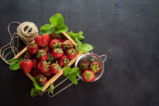 Fresh tasty strawberries in wooden box on black background.